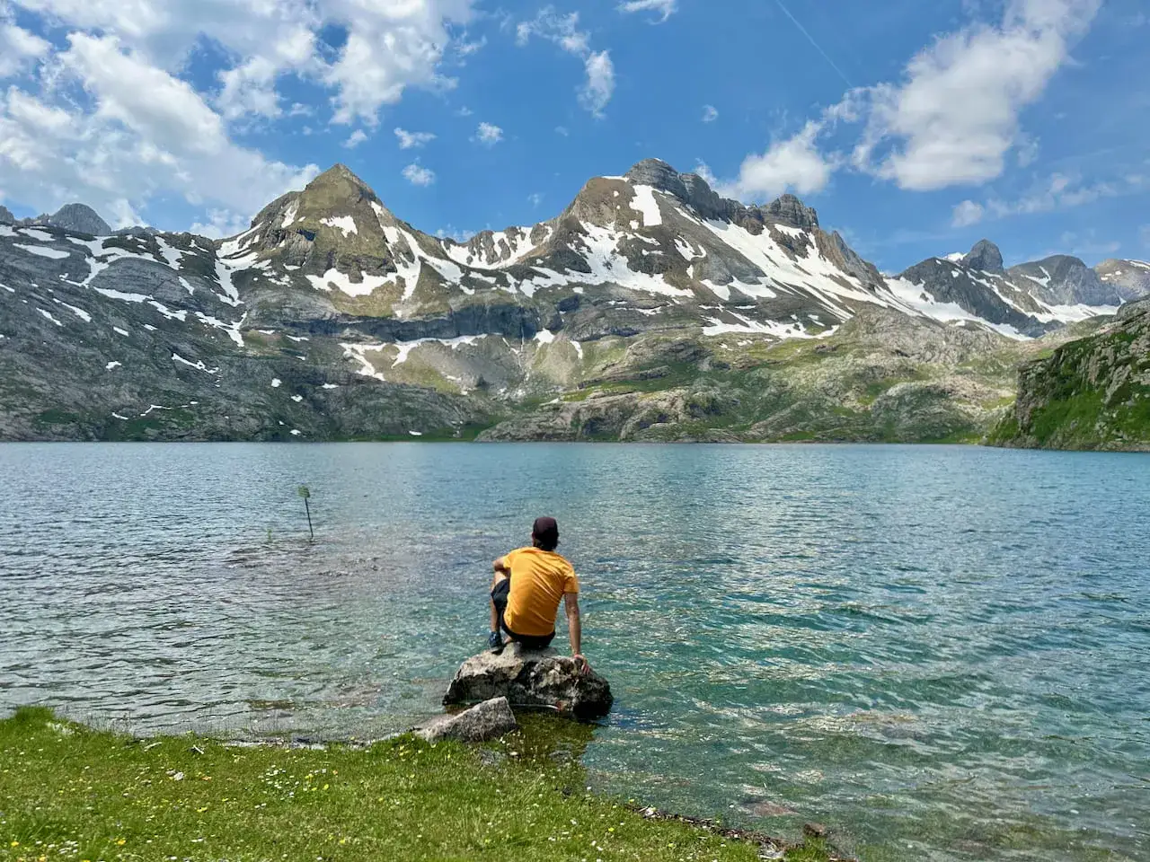 Persona sentada en roca junto al ib&oacute;n de Estan&eacute;s, contemplando las monta&ntilde;as nevadas bajo un cielo azul con nubes.
