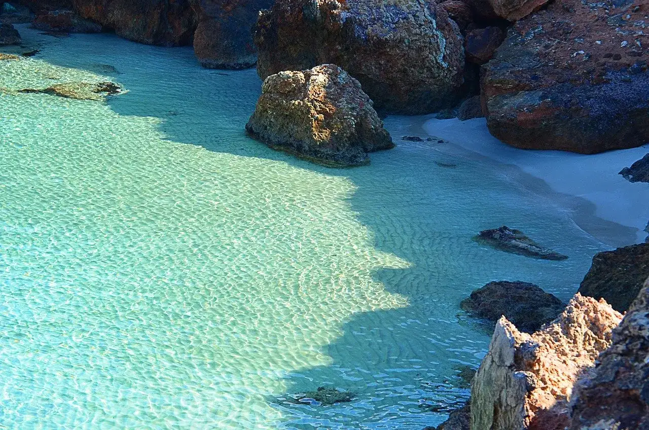 Aguas cristalinas y arena dorada en Cala d'en Carlos, rodeada de rocas imponentes.