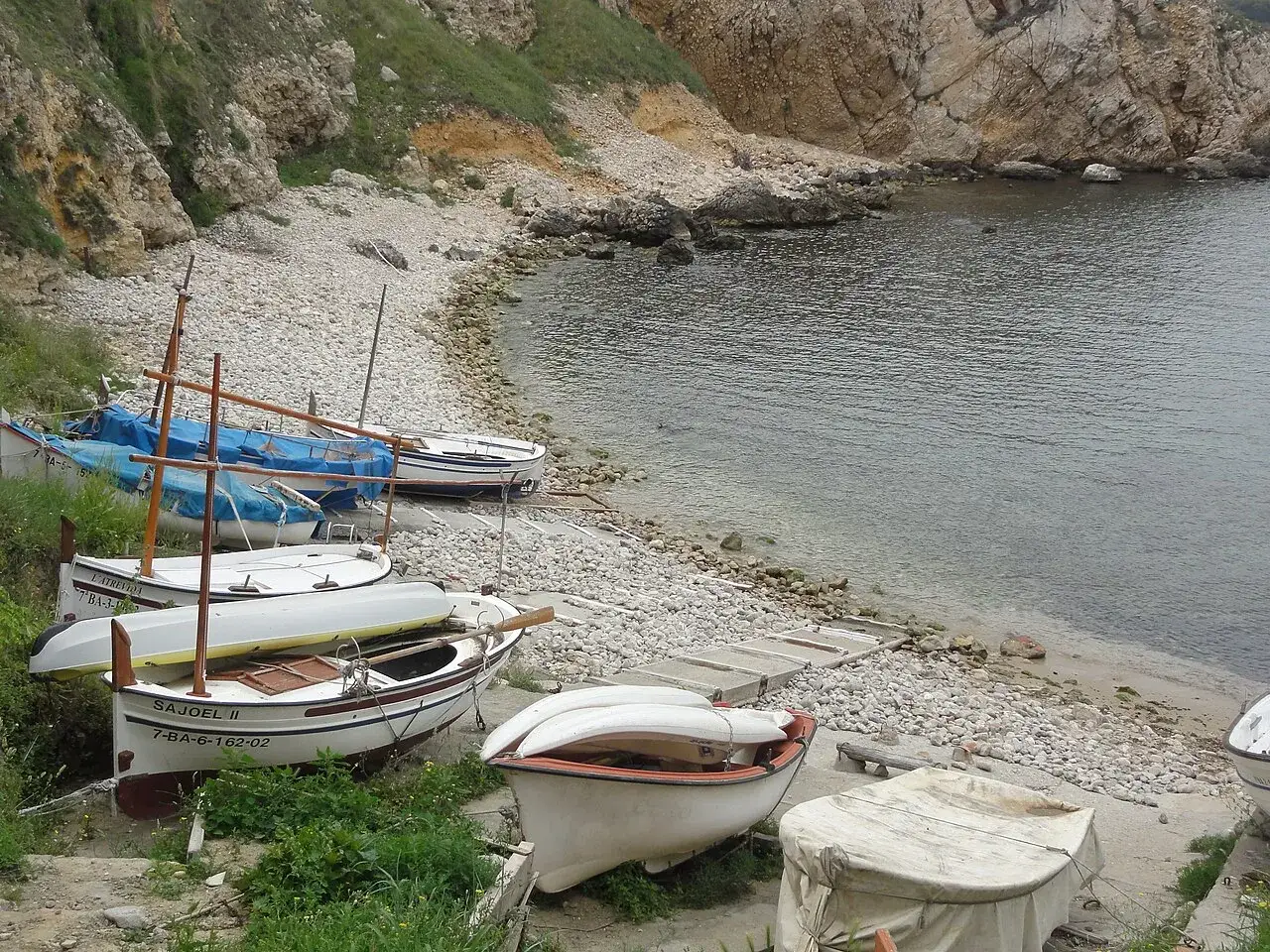 Pequeñas embarcaciones descansan en la grava de la platja cala de la creu, esperando la marea.