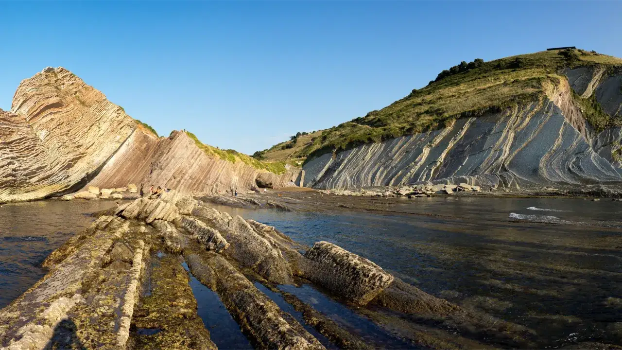 El cam&iacute; de ronda l'Escala revela formaciones rocosas estratificadas y el mar azul bajo un cielo despejado.