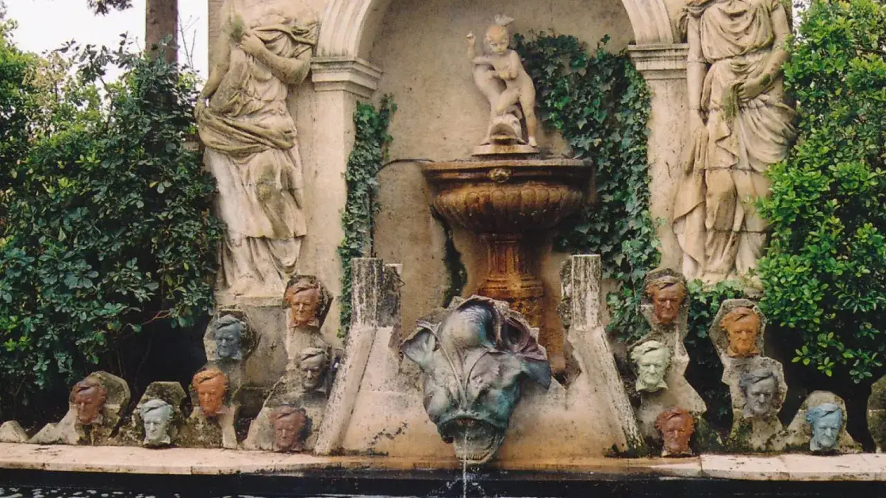 Fuente con estatuas y cabezas de piedra, evocando un antiguo castell de gala.