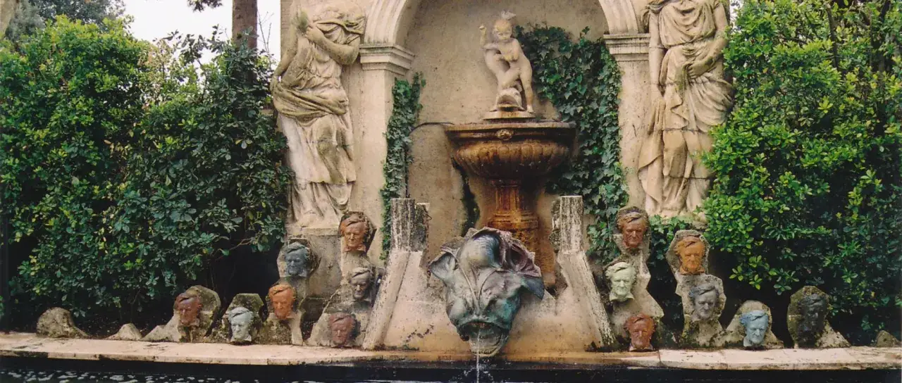Fuente con estatuas y bustos, evocando un jardín de un castillo de gala.
