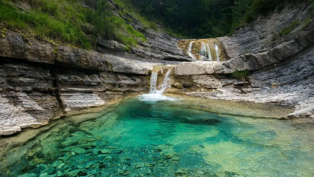 Cascada en un valle de hecho con agua turquesa cristalina y rocas estratificadas.