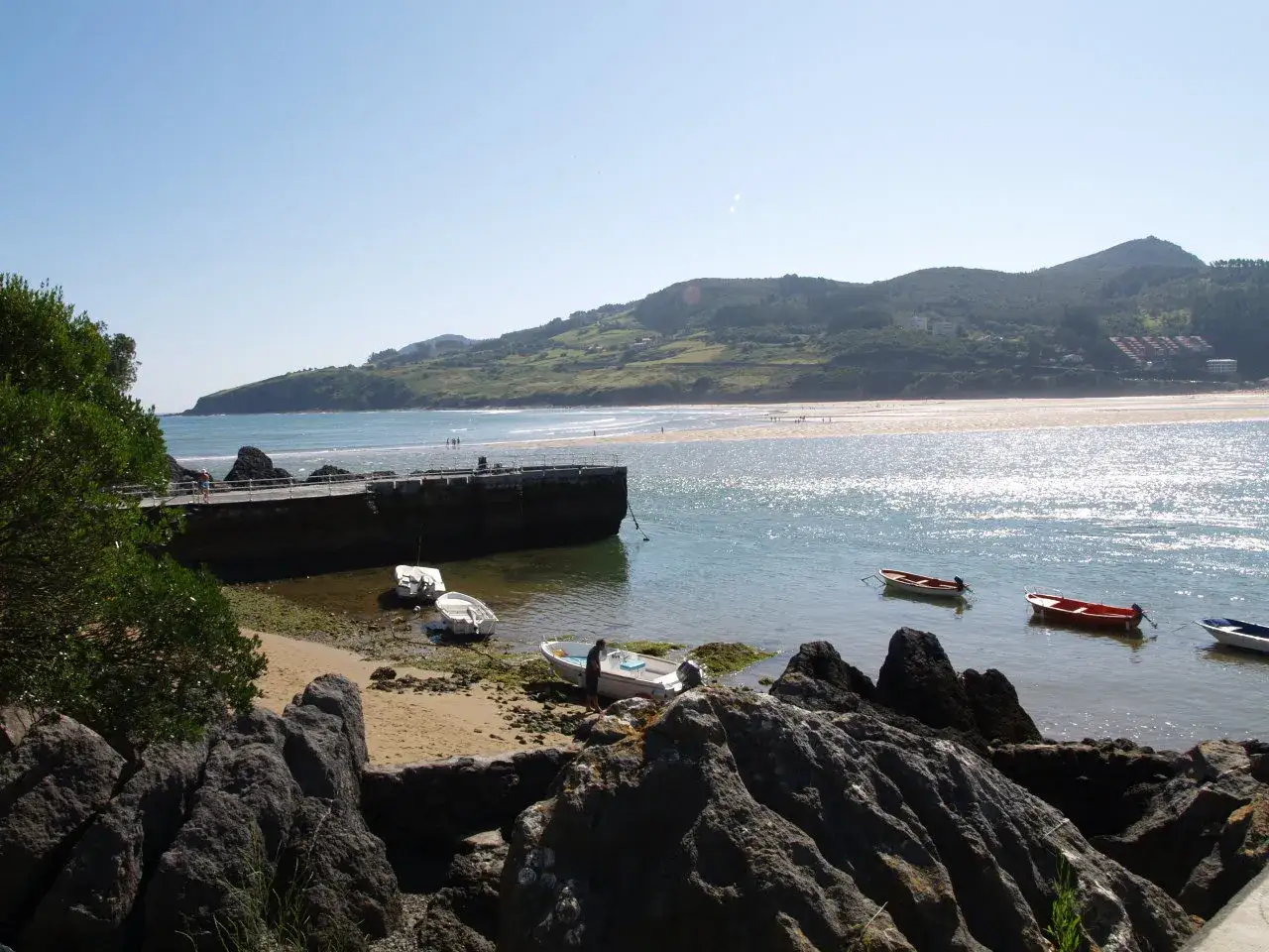 Disfruta de un día perfecto para comer en Mundaka, con barcas en la bahía y colinas verdes de fondo.