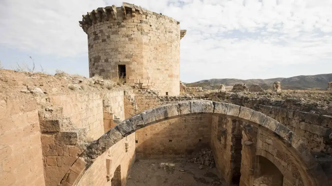 Ruinas del castillo de Mesones de Isuela, con una torre circular y un arco de piedra en primer plano.