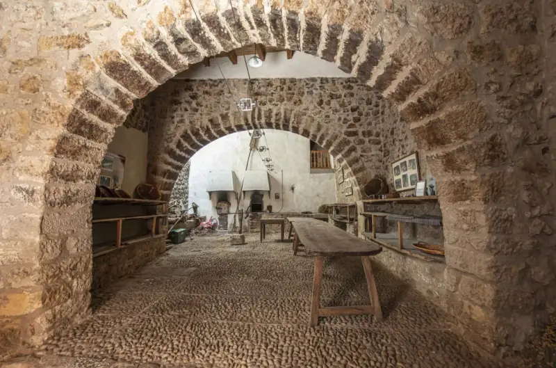 Interior de la torre de las arcas, con arcos de piedra, estanterías rústicas y un horno antiguo.