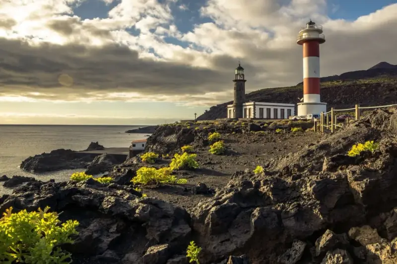 Faros gemelos en la costa rocosa, un destino que ver en La Palma. El mar y el cielo nublado completan la escena.