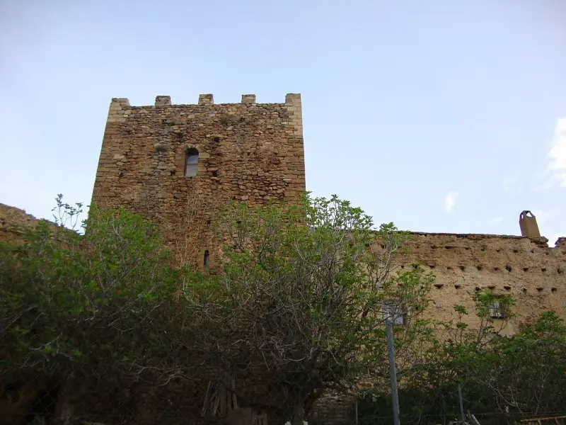 Castillo de piedra con almenas y vegetación frondosa delante.